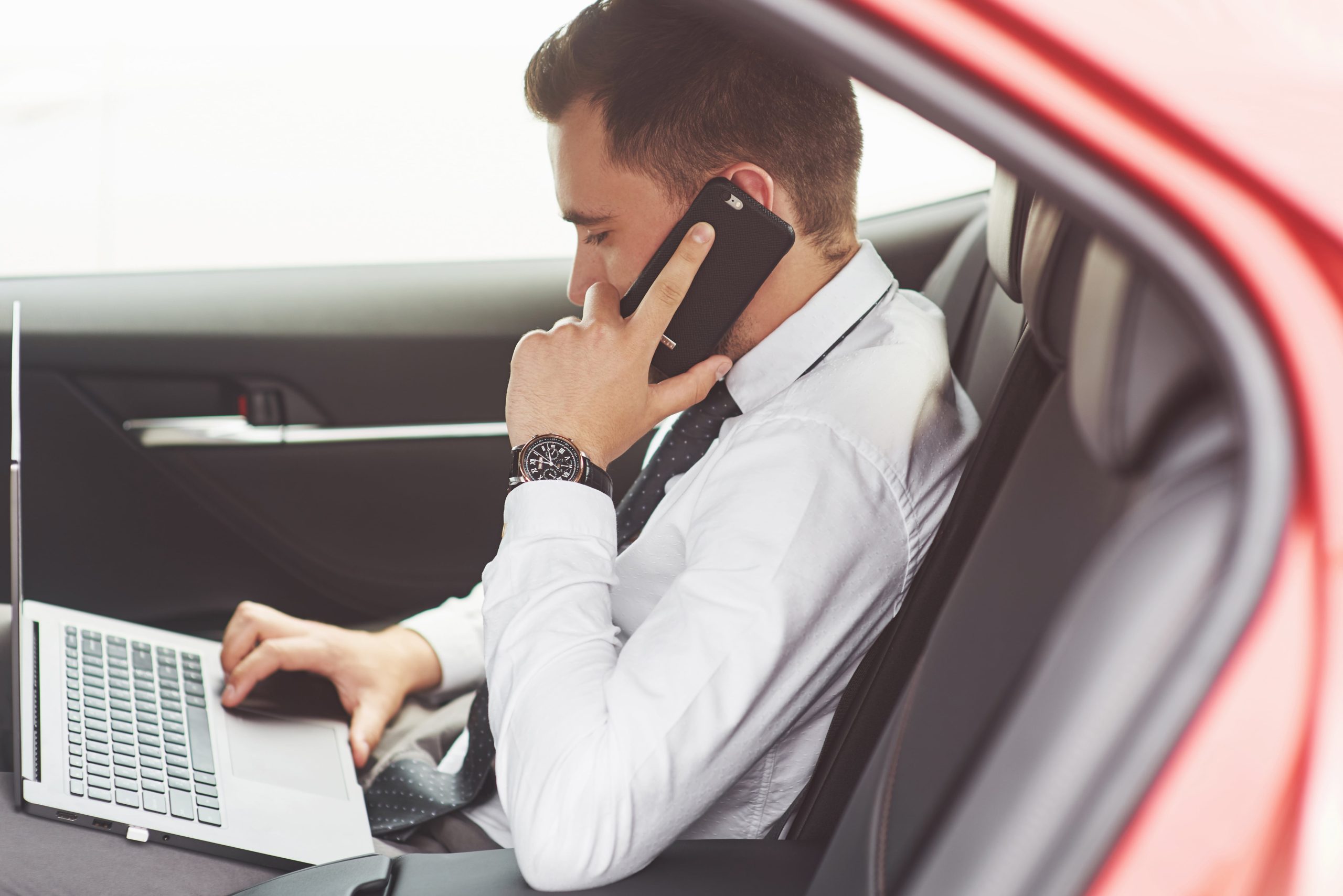 business man in car checking deductible car expenses on laptop